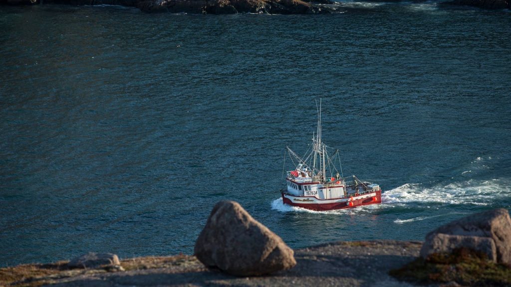 A fishing boat sails along a rocky coastline with clear waters, showcasing a tranquil seascape.